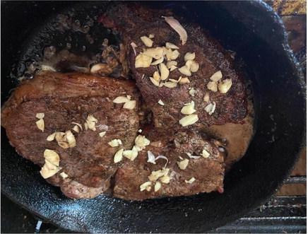 These ‘tougher’ cuts of steak have been grilled over hot coals until medium well done and now being finished in a cast iron skillet with butter and fresh garlic. Thirty minutes of slow heat will make them tender, and the butter will insure they don’t dry out. Photo by Luke Clayton