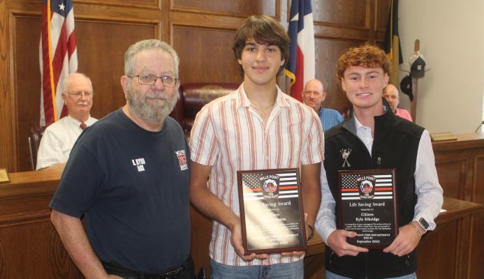 Wills Point Volunteer Fire Department Public Information Officer Kenneth Byrd (left) presented Wills Point High School seniors Yuri Frykholm and Kyle Etheridge with plaques of appreciation for their recent act of bravery. The plaques were presented during the Sept. 27 regular meeting of the Van Zandt County Commissioners Court. Photo by David Barber